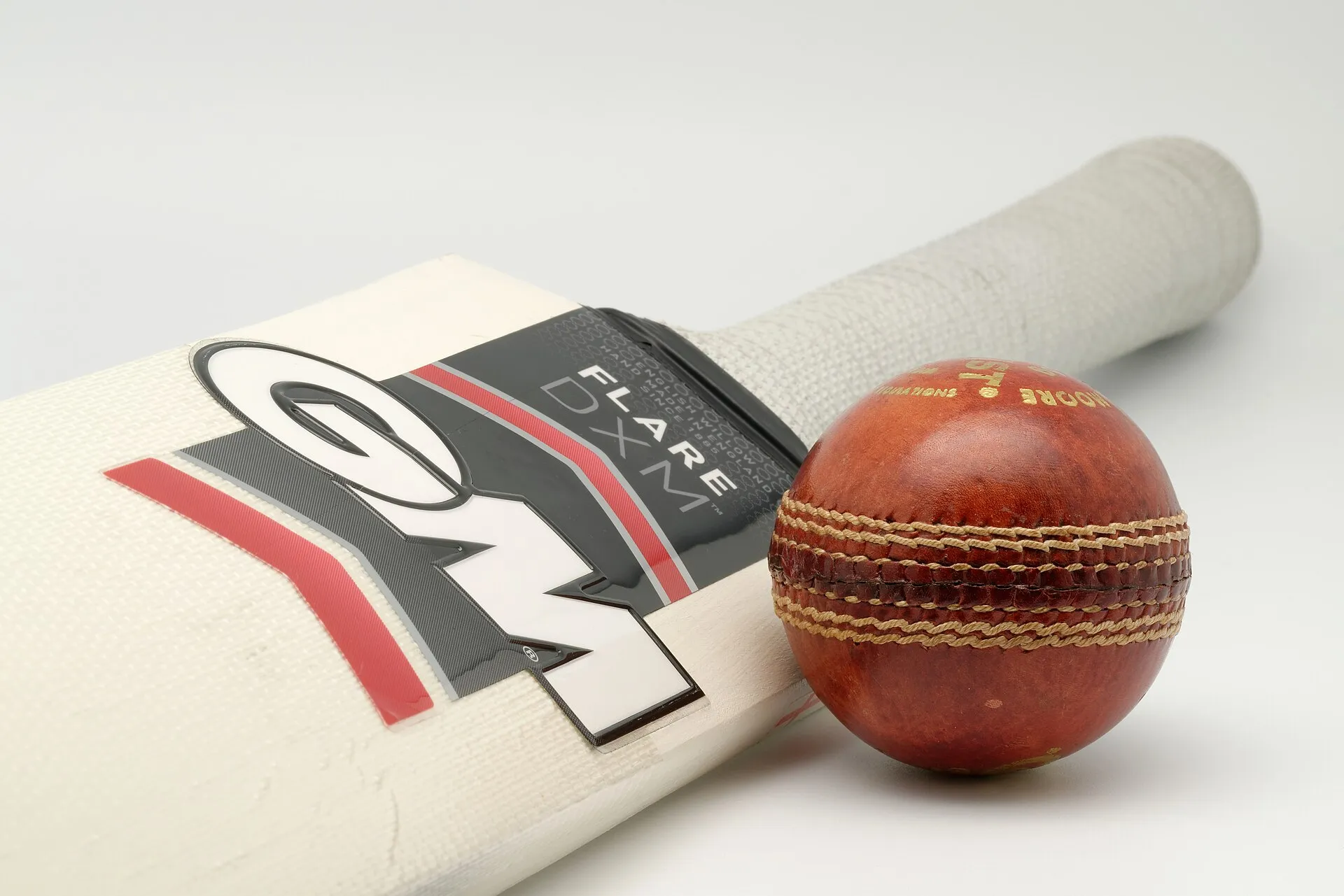 A cricket bat and a used red leather ball resting against it on a white background