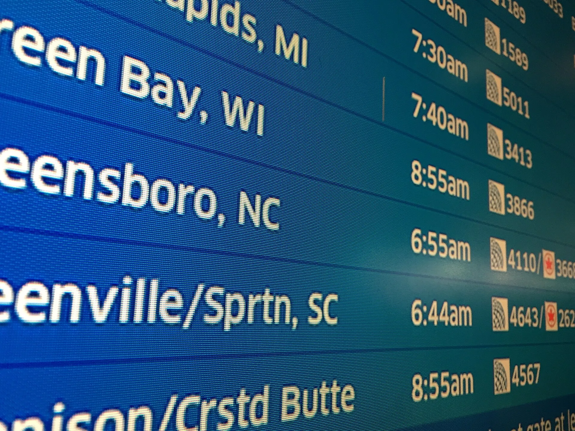 An airport departures board seen at a sharp angle, destinations and times in rows