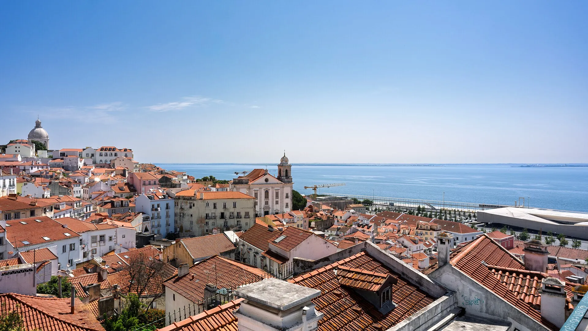 Terracotta rooftops of Alfama descending towards the Tagus estuary under a clear sky