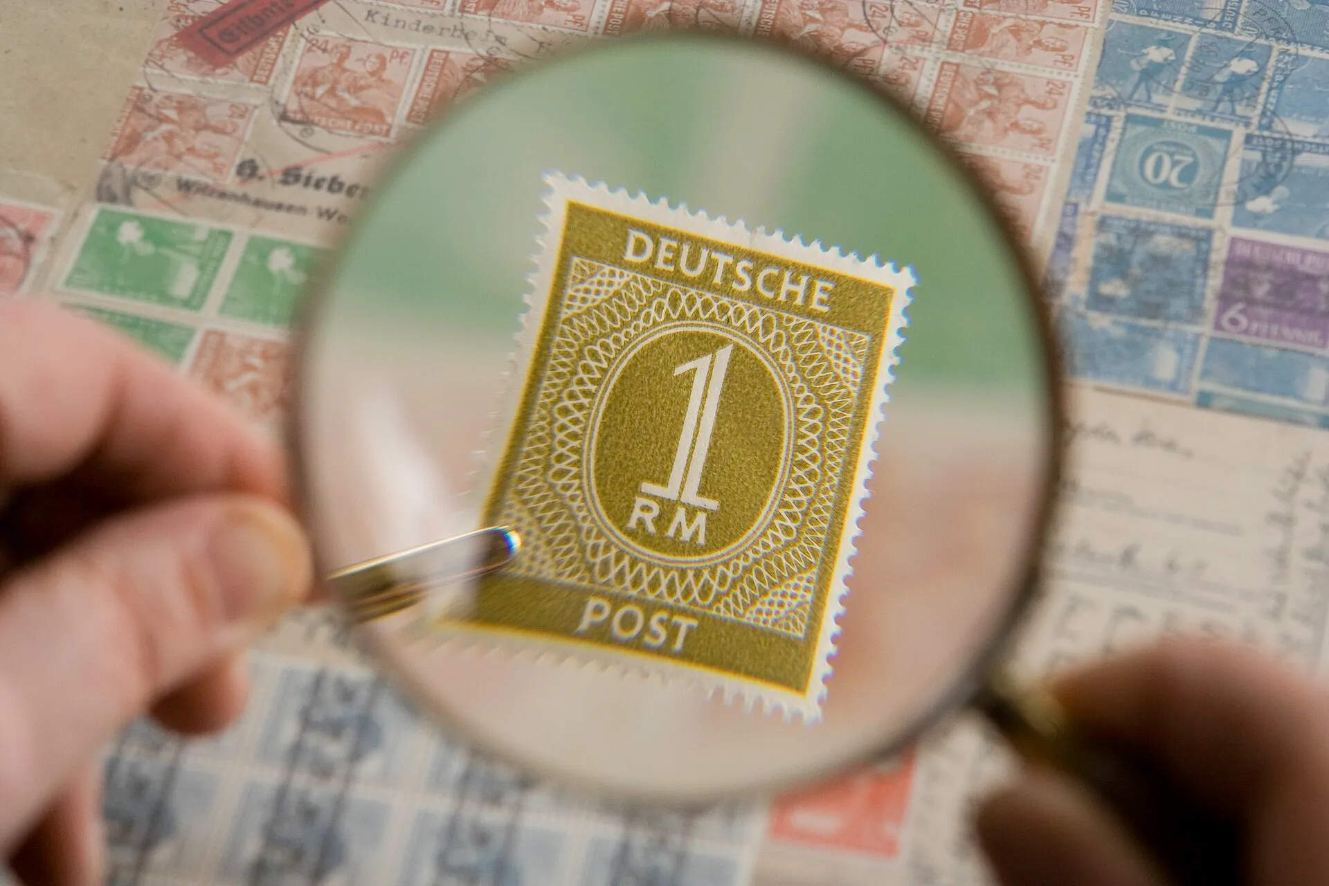 A magnifying glass held over a page of postage stamps, one stamp enlarged in the lens