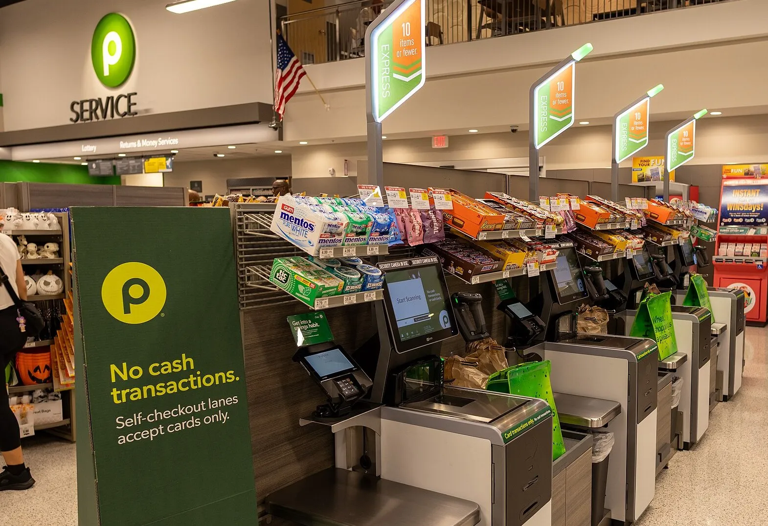 A bank of empty supermarket self-checkout lanes, with the staffed service desk visible behind them